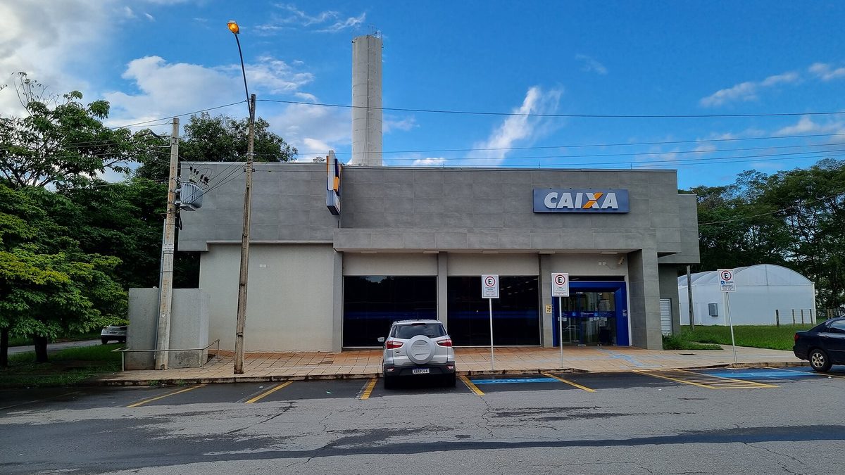 Fachada de agência da Caixa Econômica Federal com estacionamento, sob céu azul