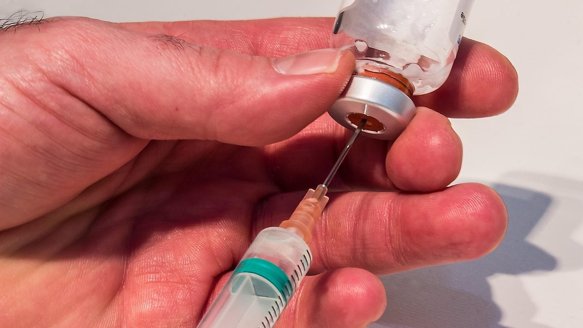 Agulha de seringa perfura a tampa de um frasco com medicamento em pó