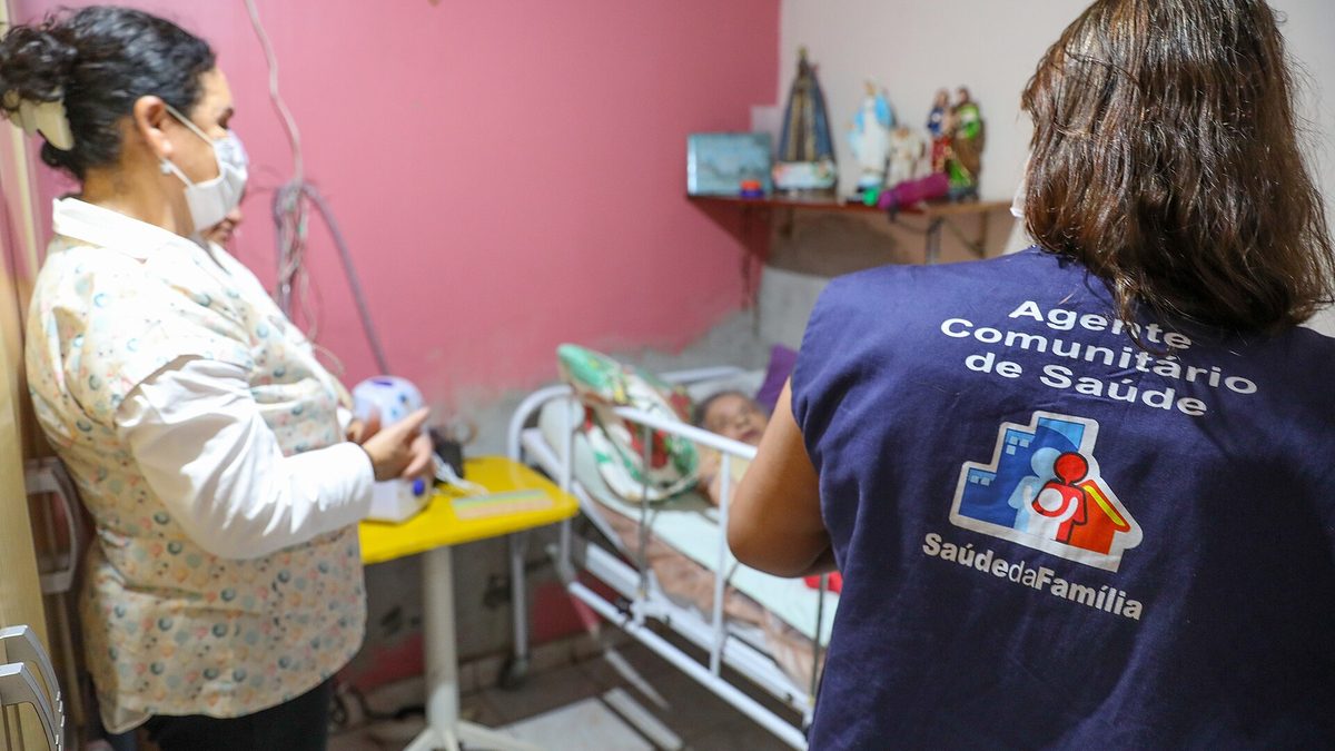 Agente comunitária de saúde, de colete azul, em visita a uma casa atendida pelo Saúde da Família