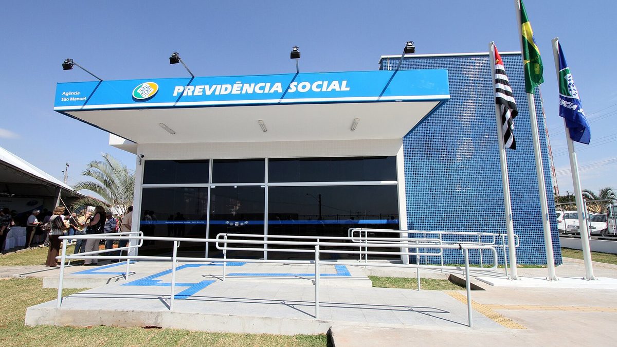 Fachada da agência da Previdência Social de São Manuel (SP), com letreiro azul e bandeiras hasteadas