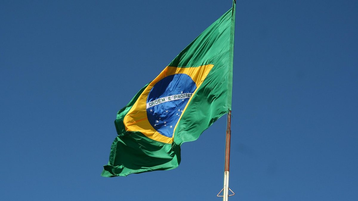 Bandeira do Brasil tremulando no alto de um mastro, contra o céu azul
