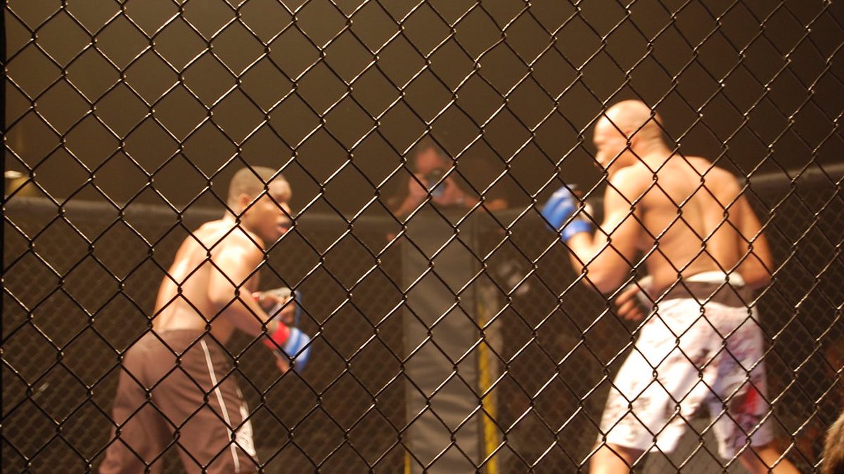 Dois lutadores de MMA se estudam dentro de uma gaiola, vistos através da grade