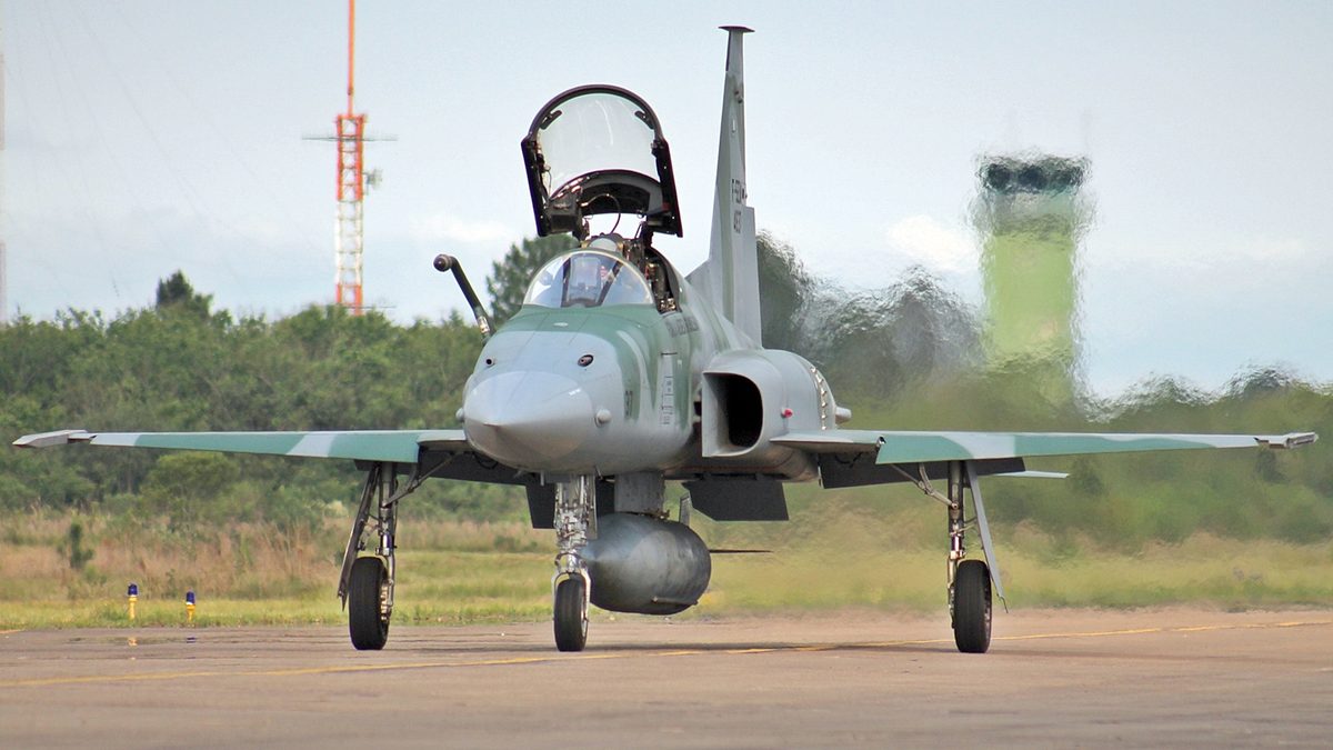 Caça F-5 da Força Aérea Brasileira na pista, com torre de controle ao fundo