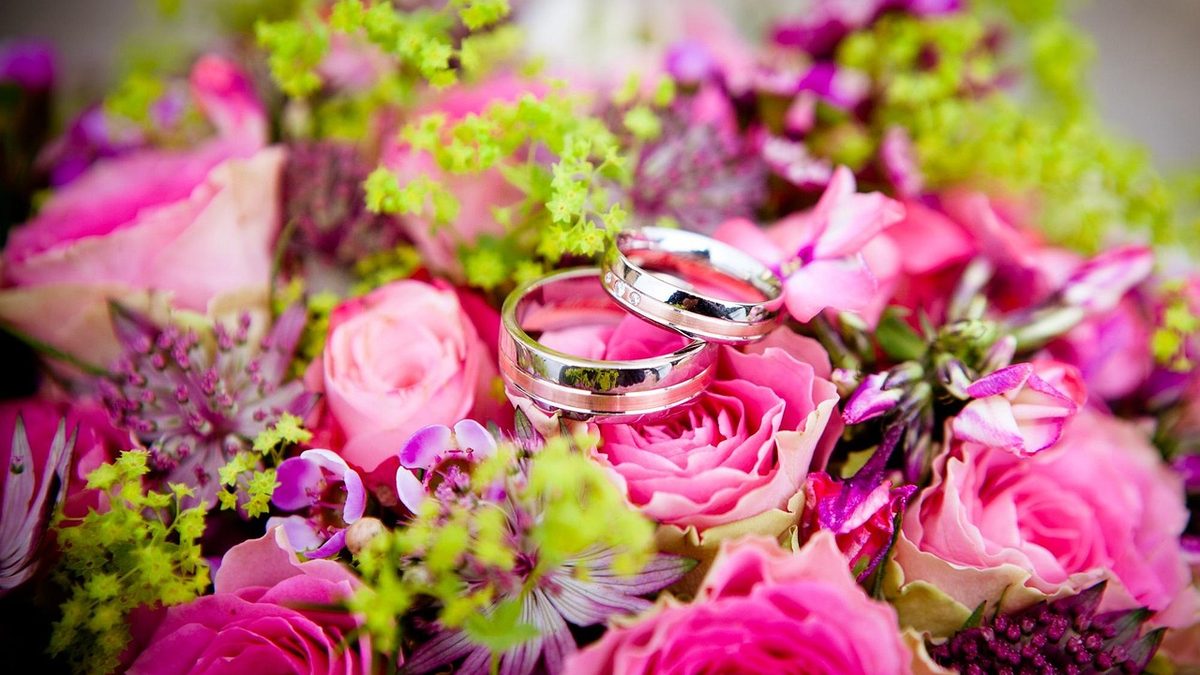 Alianças de casamento sobre buquê de rosas cor-de-rosa
