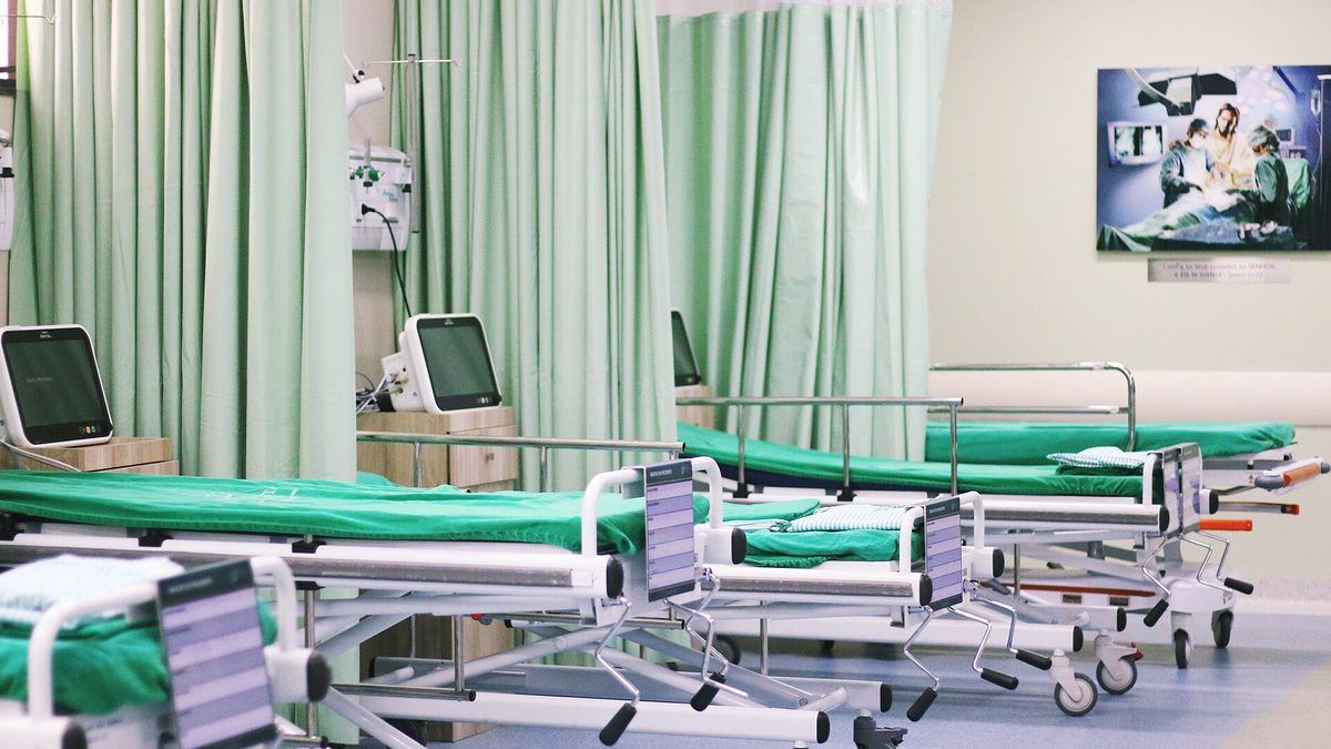 Leitos com monitores e cortinas verdes em sala de recuperação de hospital
