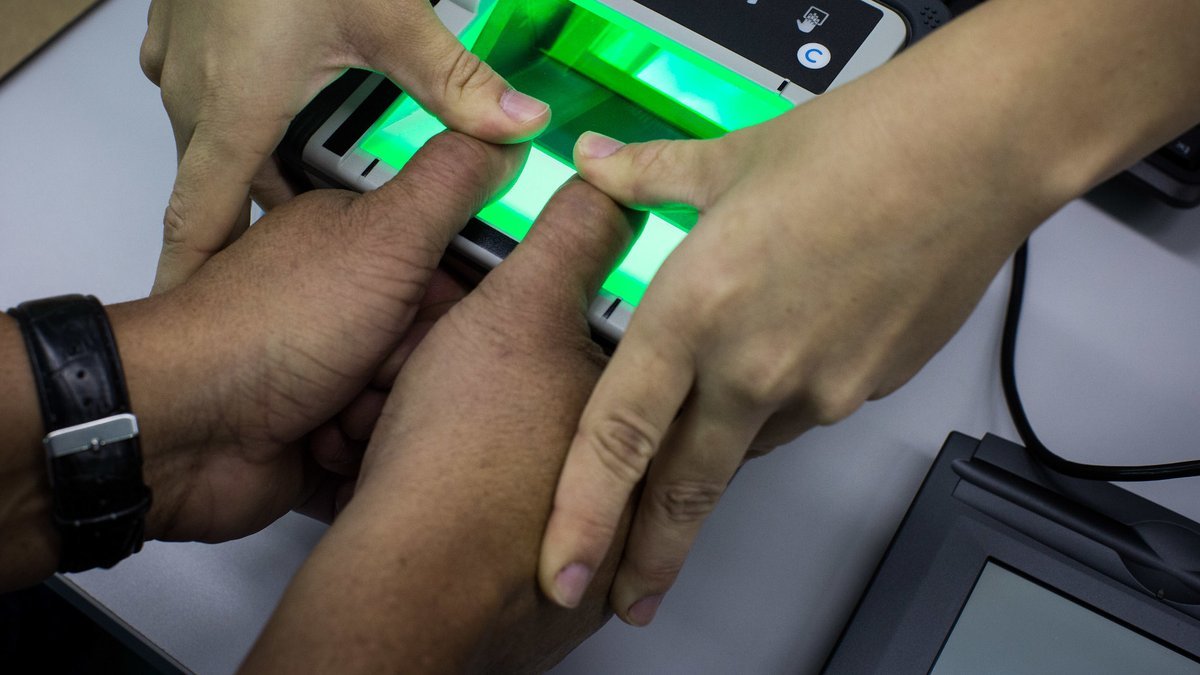 Mãos de candidato sobre leitor biométrico de digitais, com luz verde