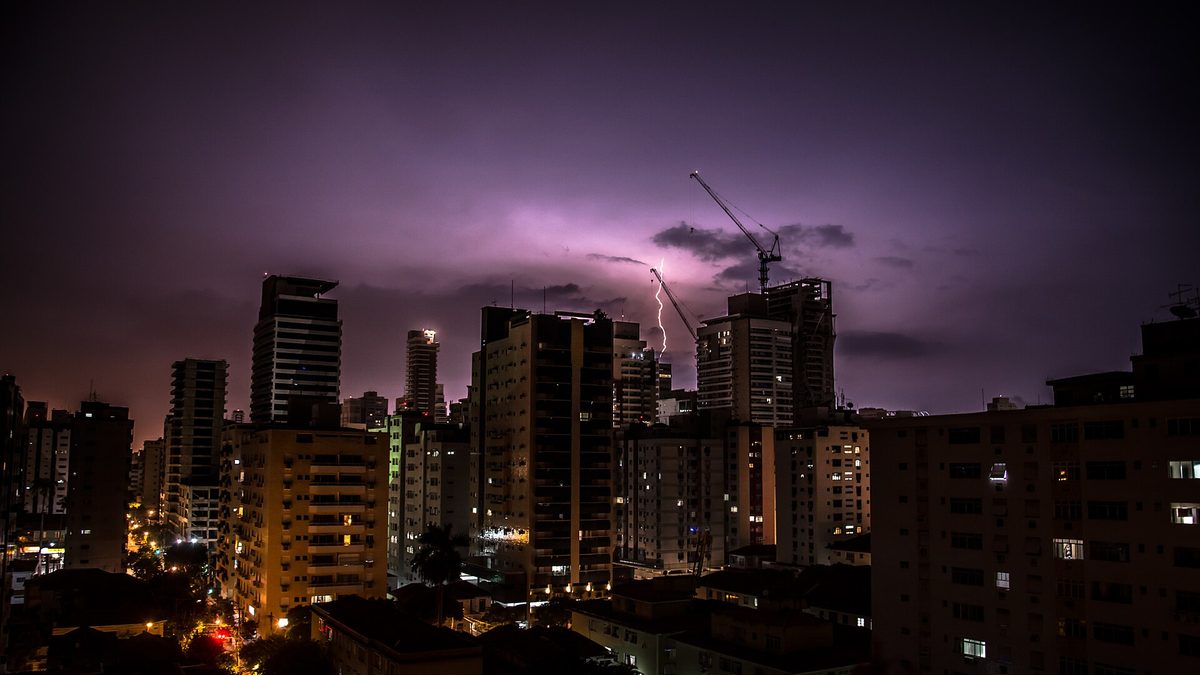 Raio cai entre prédios iluminados de Santos durante tempestade noturna