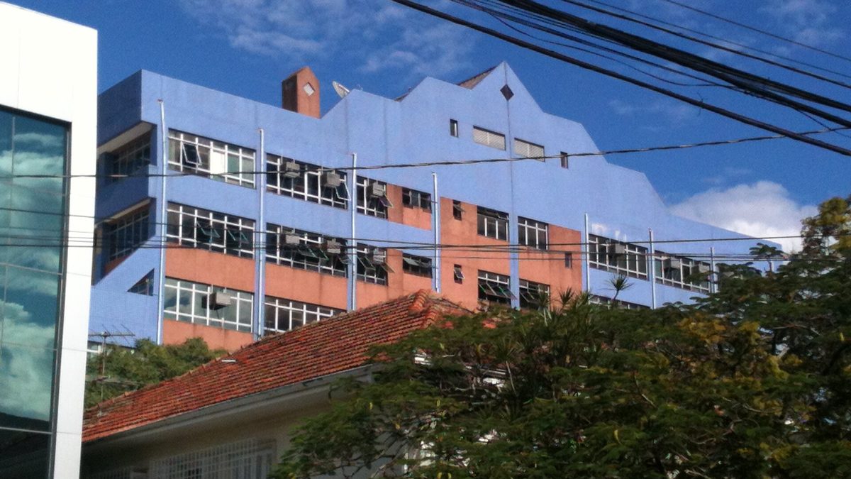 Prédio azul e salmão do Foro Trabalhista de Porto Alegre, visto por trás de árvores e telhados