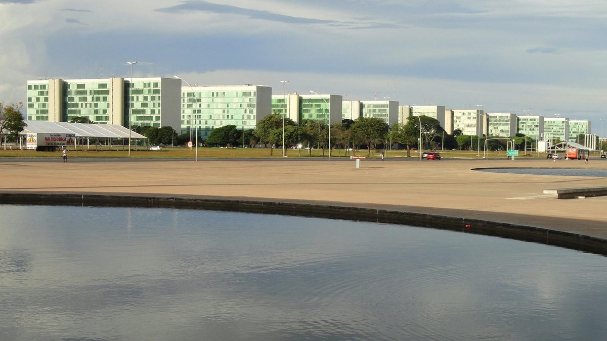 Prédios dos ministérios enfileirados na Esplanada dos Ministérios, em Brasília, com espelho d’água à frente