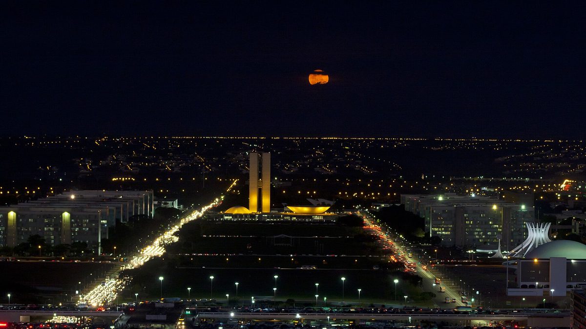 Esplanada dos Ministérios e Congresso Nacional iluminados à noite, com a Lua ao fundo, em Brasília