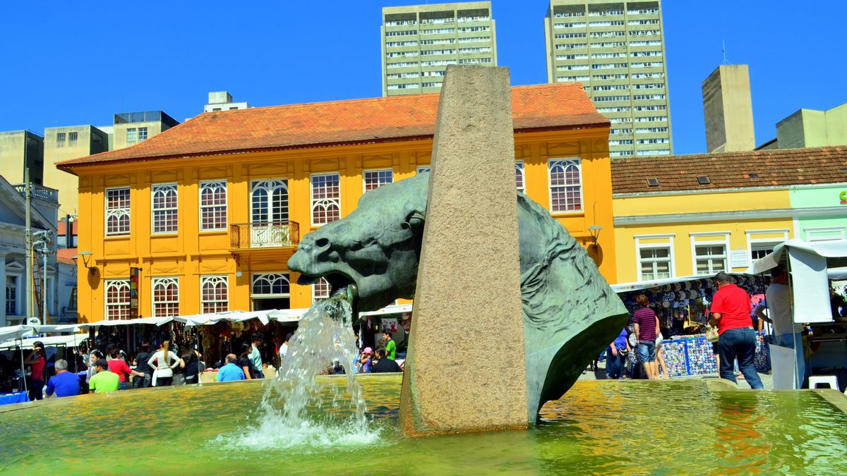 Chafariz com cabeça de cavalo no Largo da Ordem, com barracas da feira ao fundo, em Curitiba