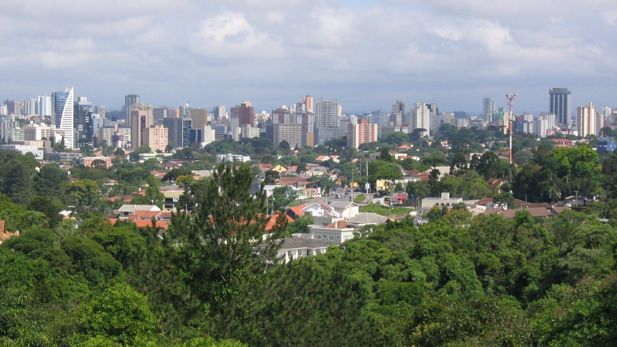 Prédios de Curitiba vistos ao longe, atrás de uma área verde com árvores