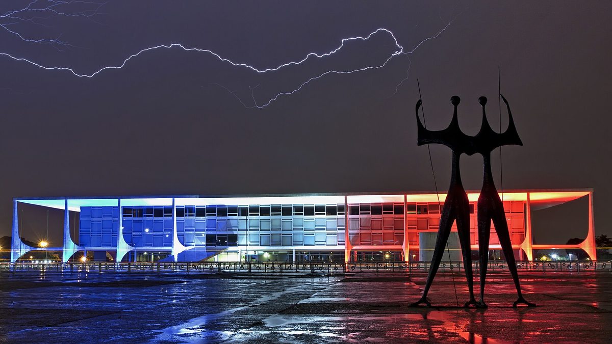 Palácio do Planalto iluminado à noite, com a escultura Os Candangos na Praça dos Três Poderes e um raio no céu