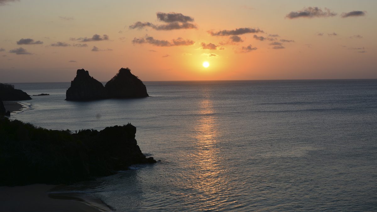 Pôr do sol no mar com o Morro Dois Irmãos ao fundo, em Fernando de Noronha