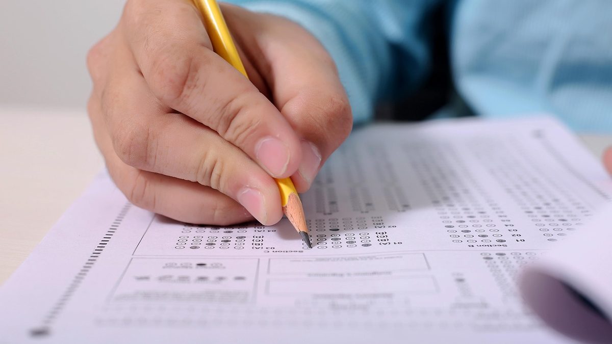 Mão preenche com lápis as bolinhas de um cartão de respostas de prova de múltipla escolha