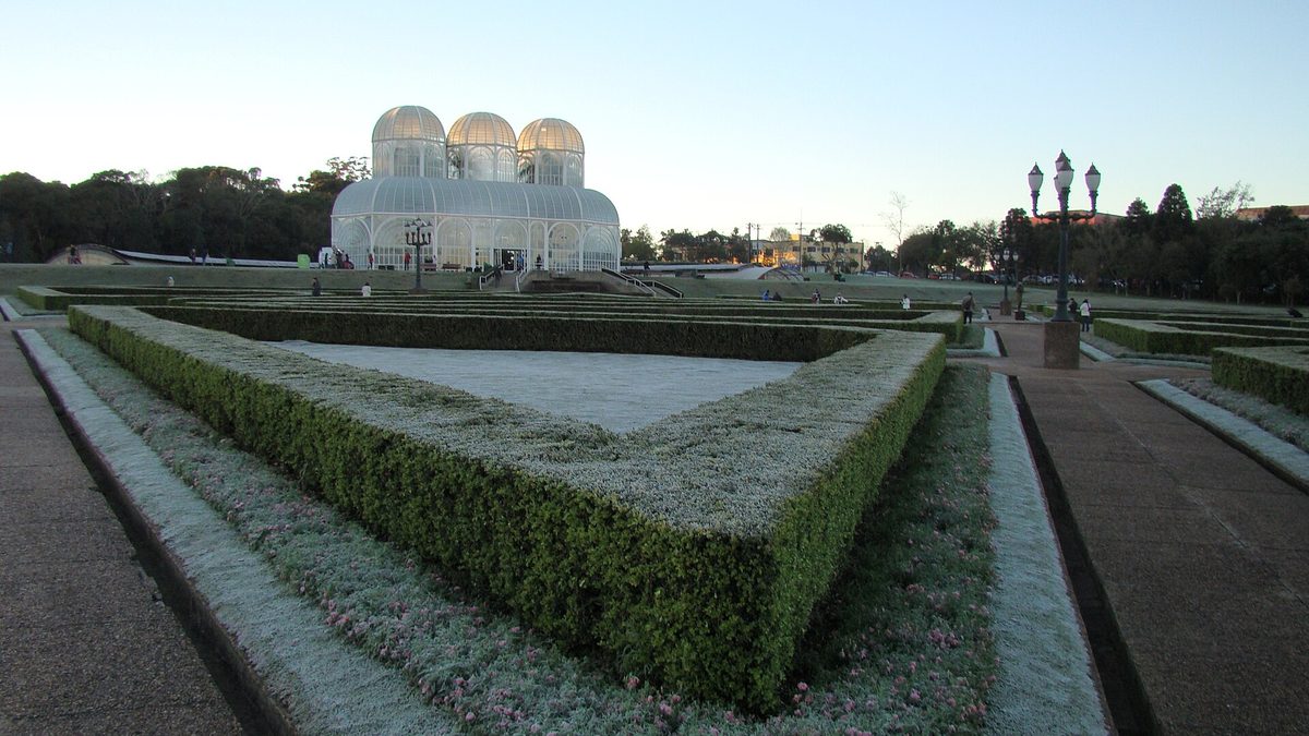 Geada sobre os canteiros do Jardim Botânico de Curitiba, com a estufa ao fundo