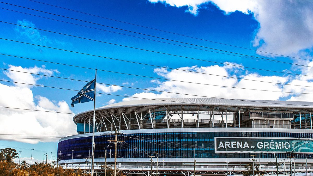 Fachada da Arena do Grêmio sob céu azul, em Porto Alegre