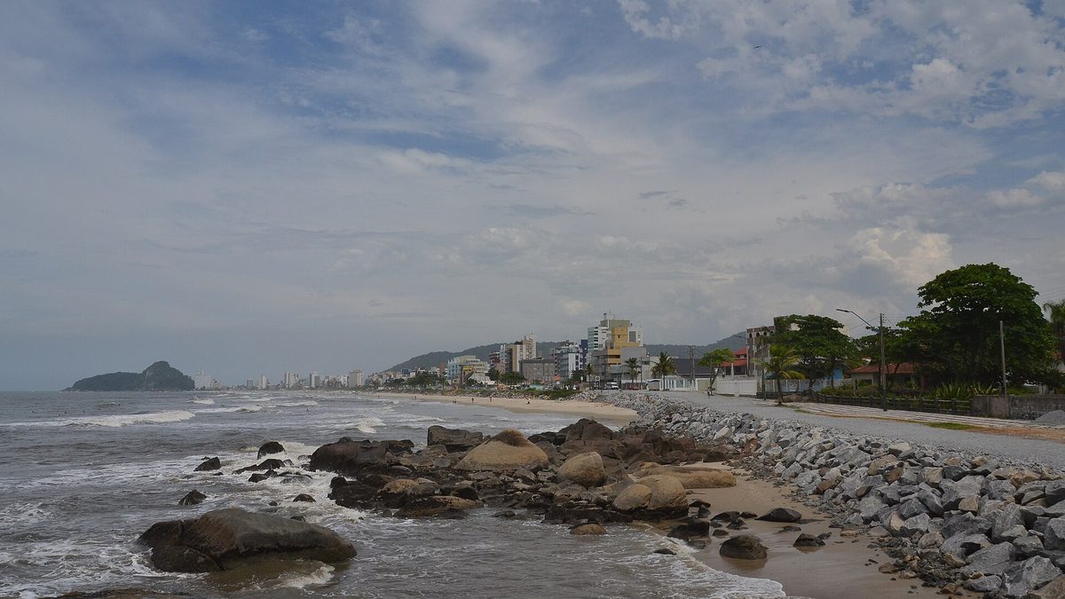 Orla de Matinhos com pedras, mar e prédios ao fundo, no litoral do Paraná