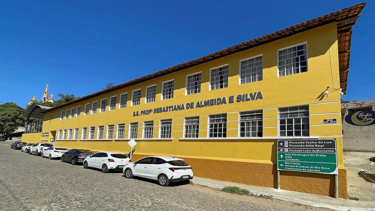 Fachada amarela de escola estadual de dois andares em Jaguaraçu (MG), com carros estacionados na rua