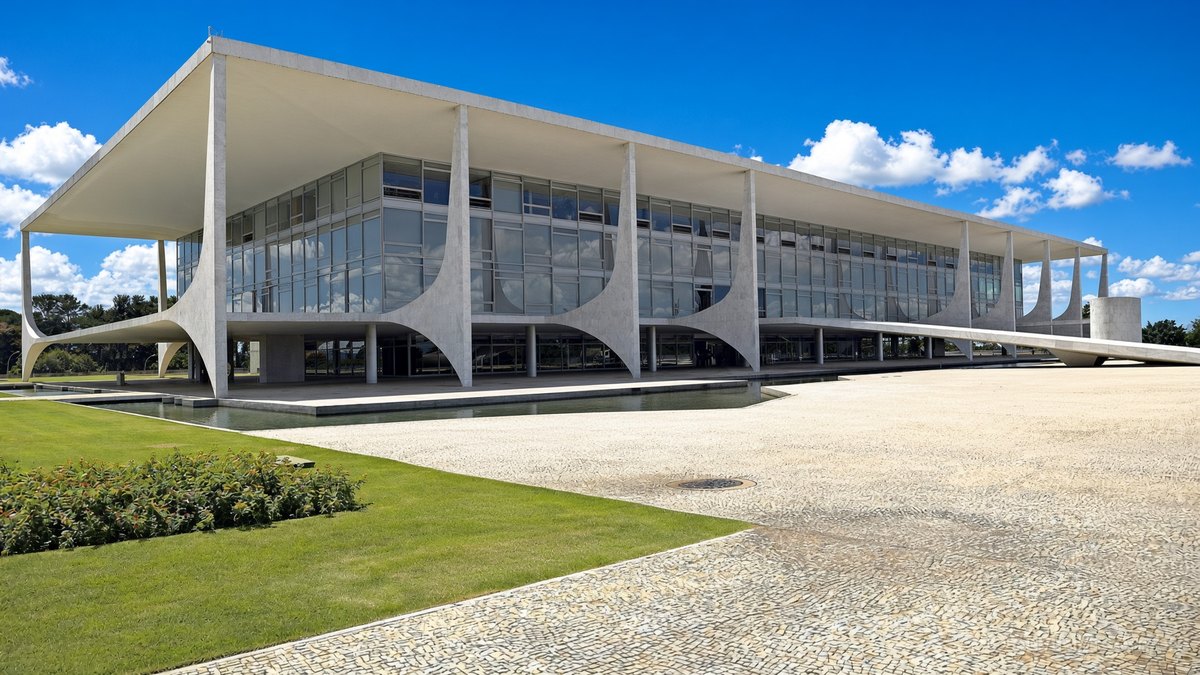 Fachada do Palácio do Planalto, com colunas curvas e espelho d’água, sob céu azul ensolarado, em Brasília