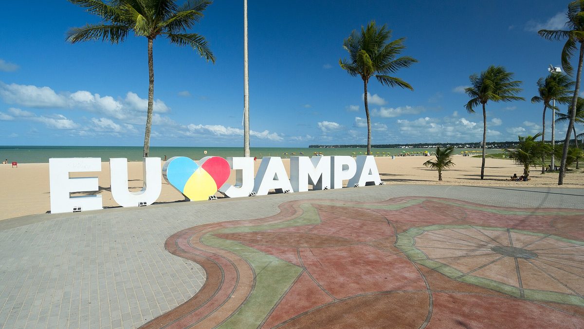 Letreiro branco Eu amo Jampa, com coração colorido, na Praia de Tambaú, em João Pessoa, com coqueiros e o mar ao fundo
