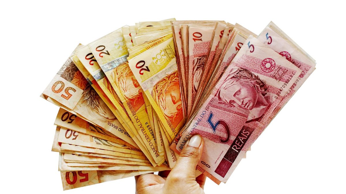 Mão segura um leque de cédulas de real de vários valores