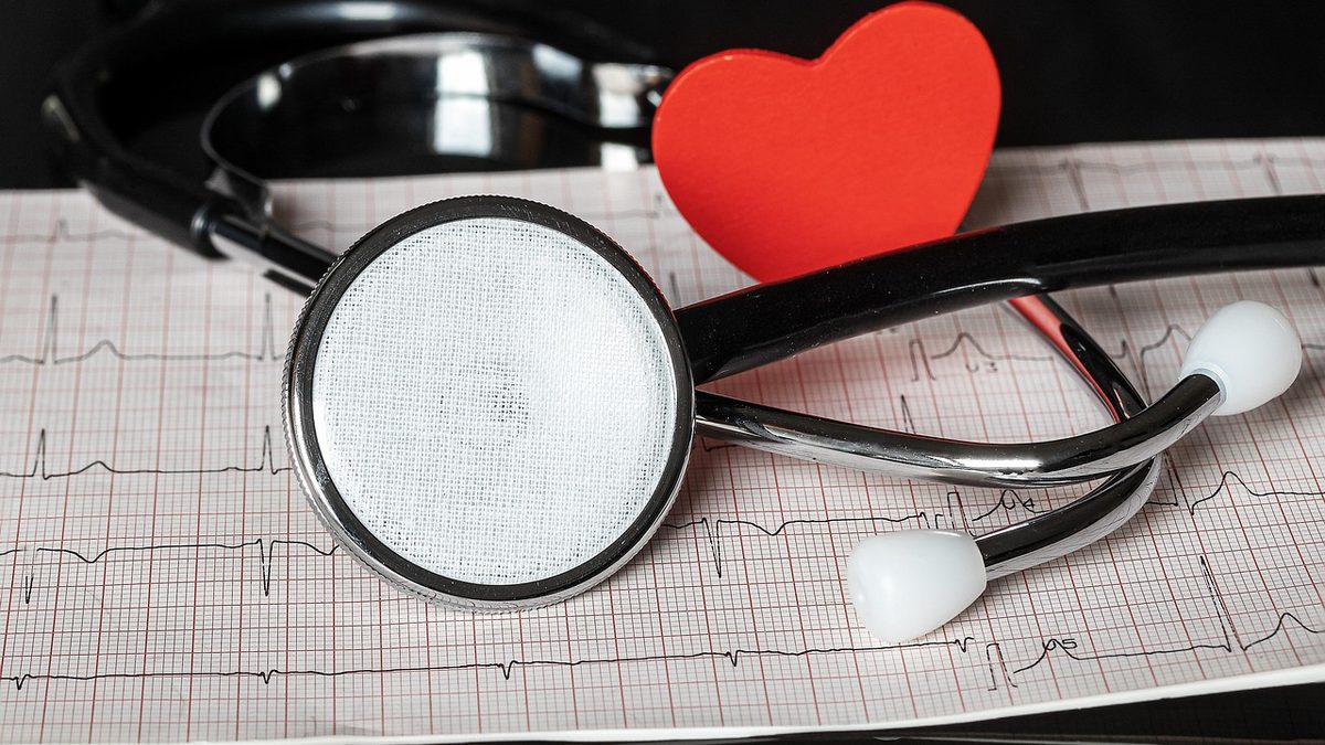 Estetoscópio sobre papel de eletrocardiograma, ao lado de um coração vermelho