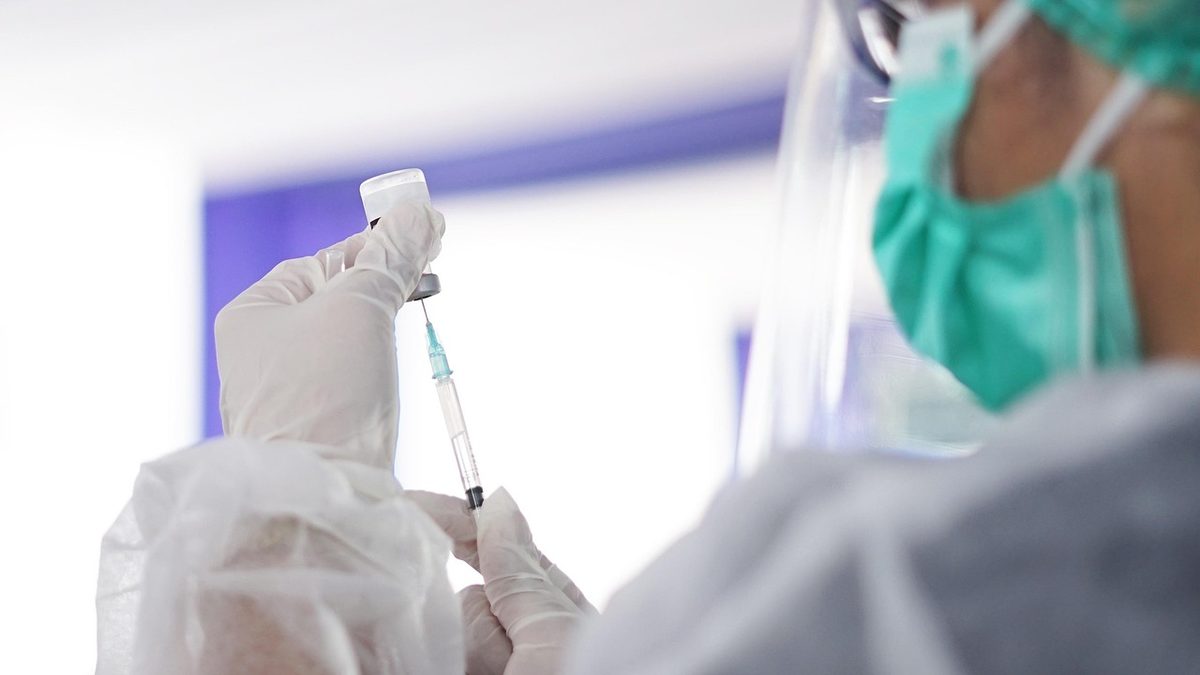 Profissional de saúde com luvas e máscara prepara dose de vacina com seringa