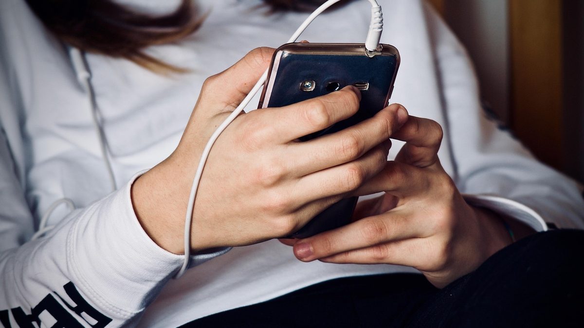 Mãos de uma pessoa segurando um celular com fone de ouvido conectado
