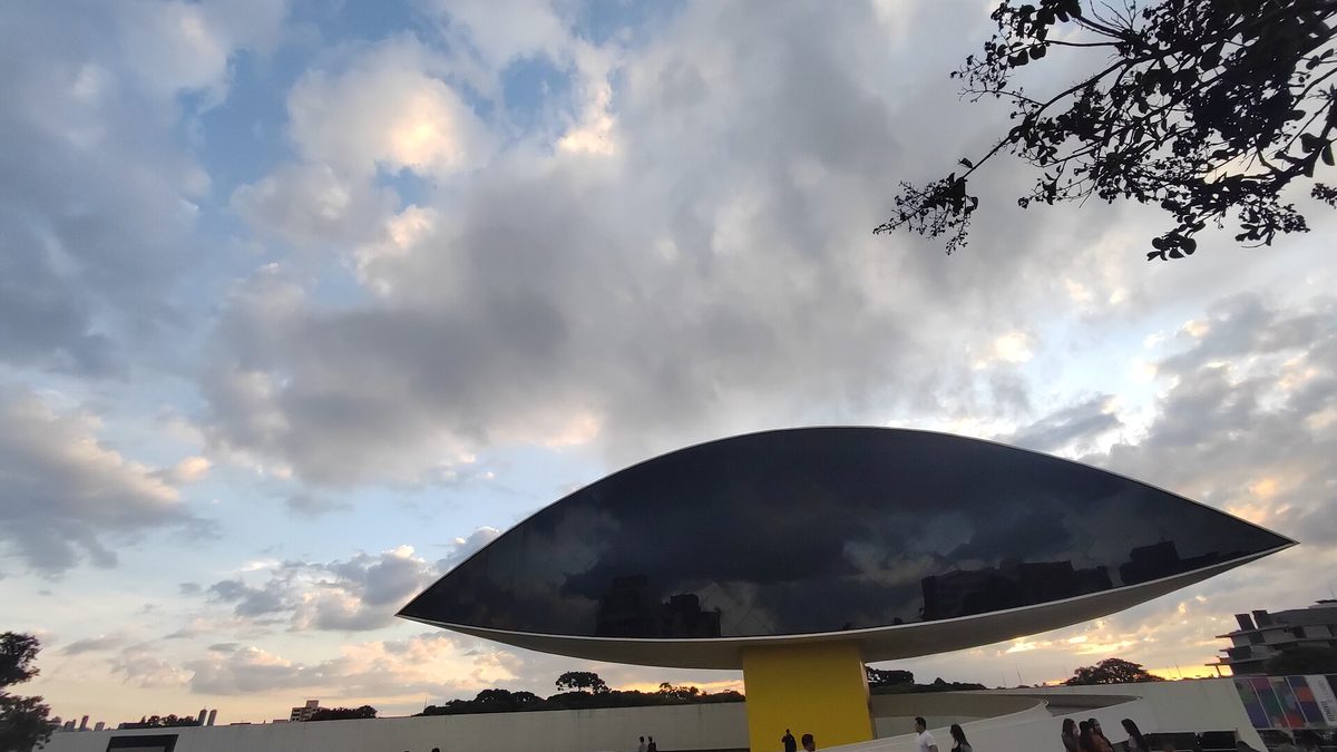 O Olho do Museu Oscar Niemeyer, com fachada de vidro escuro sobre torre amarela, em Curitiba