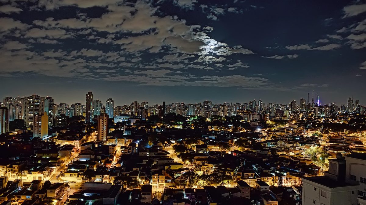 Prédios de São Paulo iluminados à noite sob céu com nuvens