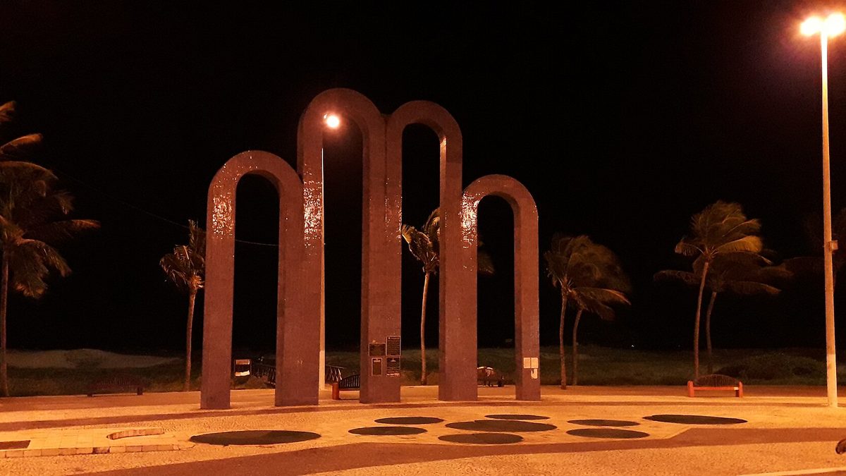 Arcos da Orla de Atalaia iluminados à noite, entre coqueiros, em Aracaju