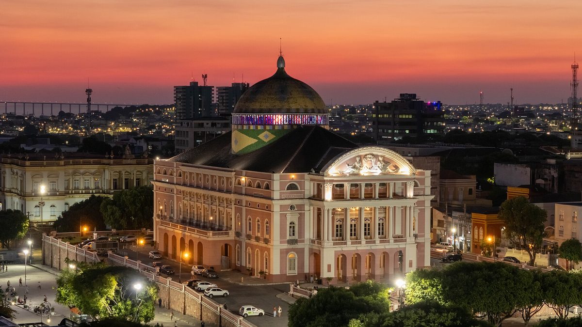 Teatro Amazonas iluminado ao entardecer, com a cúpula colorida, no centro de Manaus