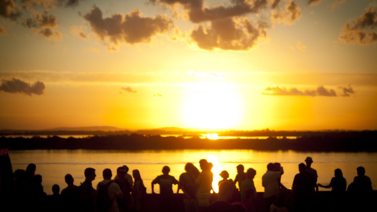 Pessoas em silhueta veem o pôr do sol sobre o Guaíba, em Porto Alegre