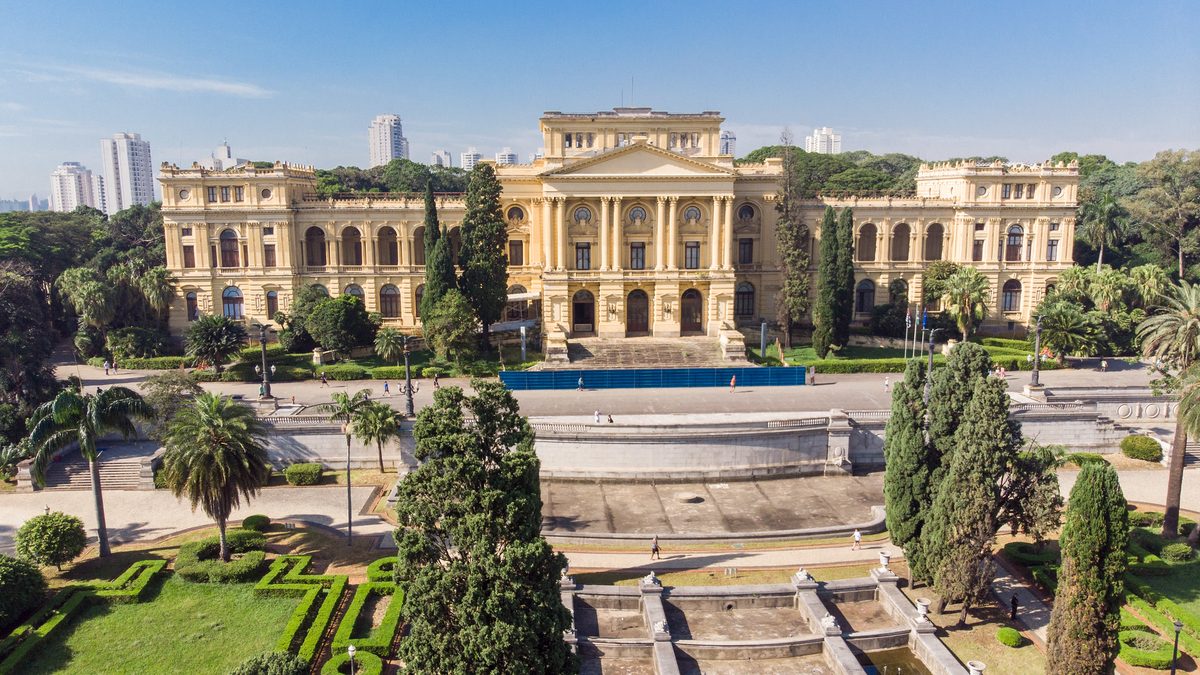 Fachada amarela do Museu do Ipiranga, em São Paulo, vista do alto, com jardins e palmeiras em frente