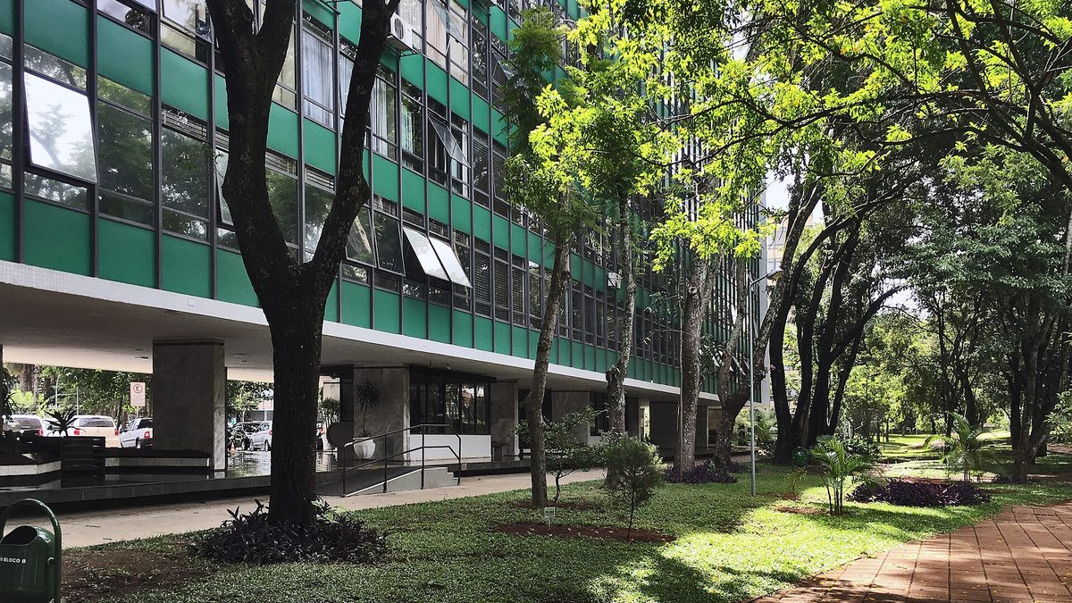 Prédio residencial sobre pilotis cercado de árvores e gramado numa superquadra de Brasília