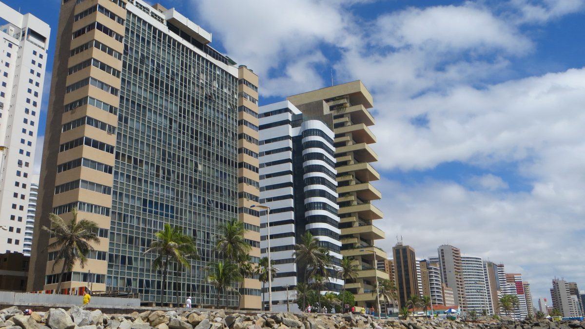 Prédios residenciais e coqueiros na orla de Fortaleza, vistos das pedras do quebra-mar