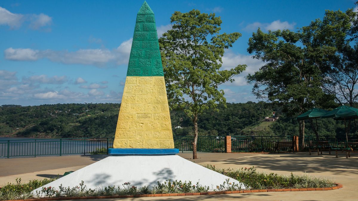 Obelisco verde e amarelo do Marco das Três Fronteiras, em Foz do Iguaçu, com o rio ao fundo