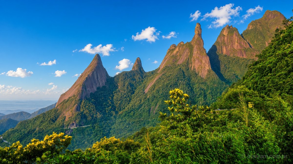 Picos de granito da Serra dos Órgãos, entre eles o Dedo de Deus, sobre a Mata Atlântica e céu azul numa manhã de sol