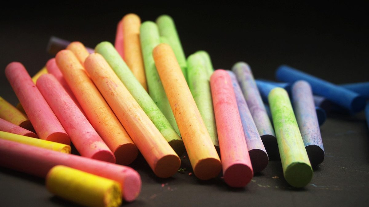 Gizes coloridos usados em sala de aula, espalhados sobre uma superfície escura
