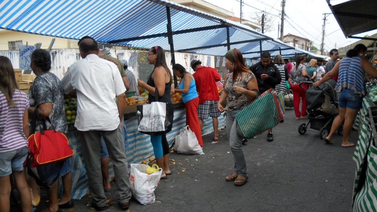 Clientes circulam entre barracas cobertas de uma feira livre em São Paulo