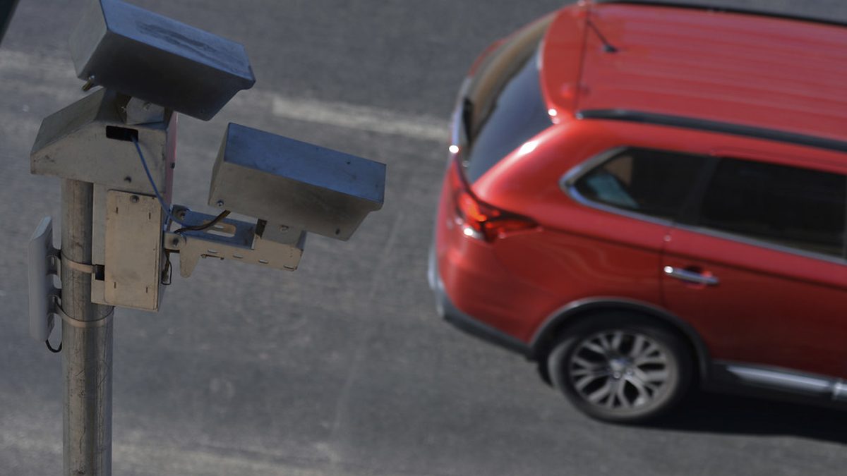 Radar de velocidade ao lado de carro vermelho em uma avenida