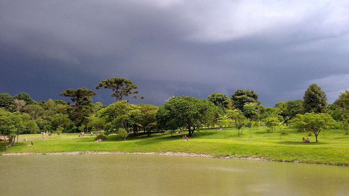 Nuvens carregadas sobre parque com lago e araucárias em Curitiba