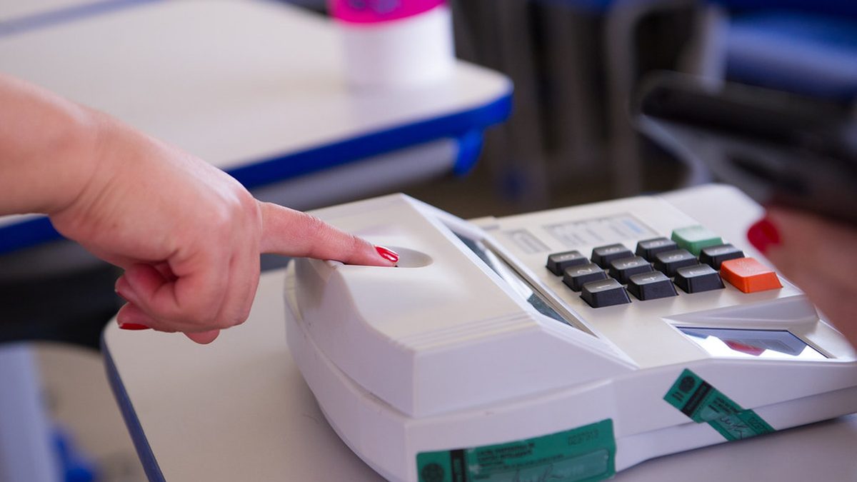 Eleitora encosta o dedo no leitor biométrico do terminal do mesário em seção eleitoral