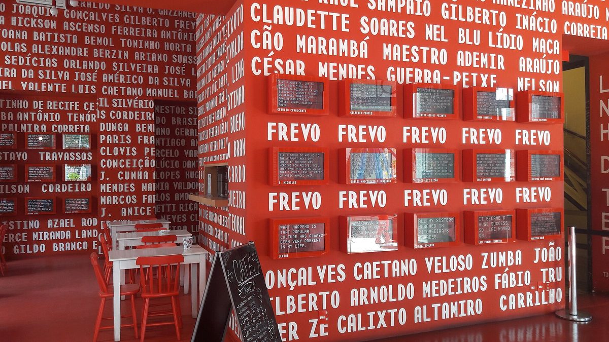 Parede vermelha com a palavra frevo e nomes de artistas no interior do Paço do Frevo, no Recife