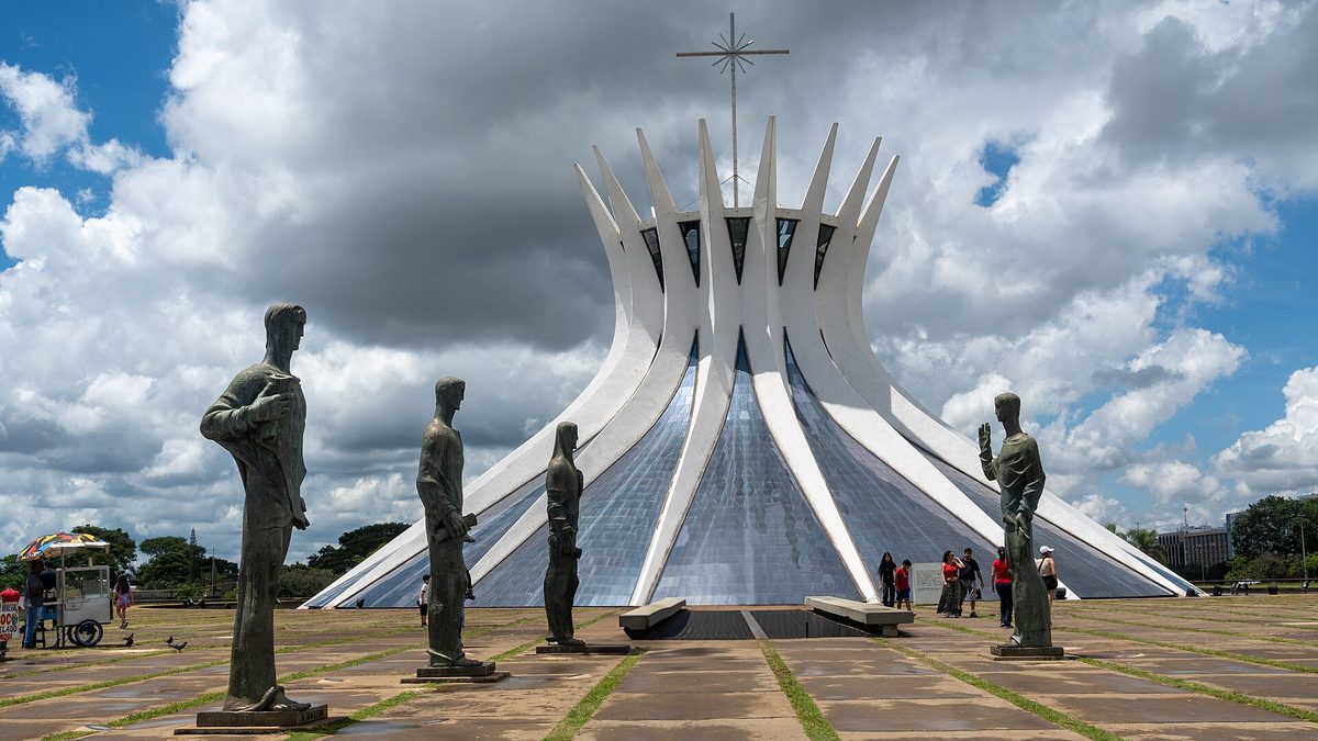 Catedral Metropolitana de Brasília e estátuas dos evangelistas na praça em frente, sob céu azul