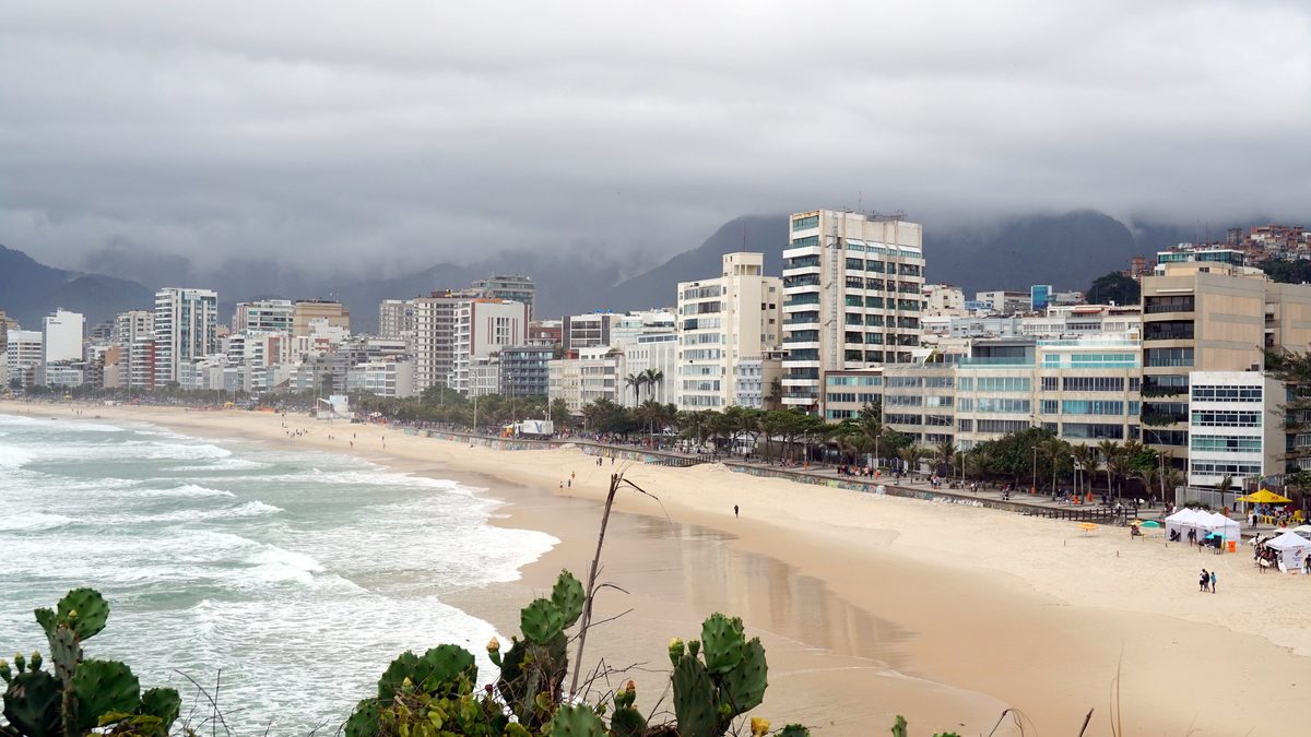 Praia de Ipanema sob nuvens carregadas, com prédios e morros ao fundo, no Rio de Janeiro