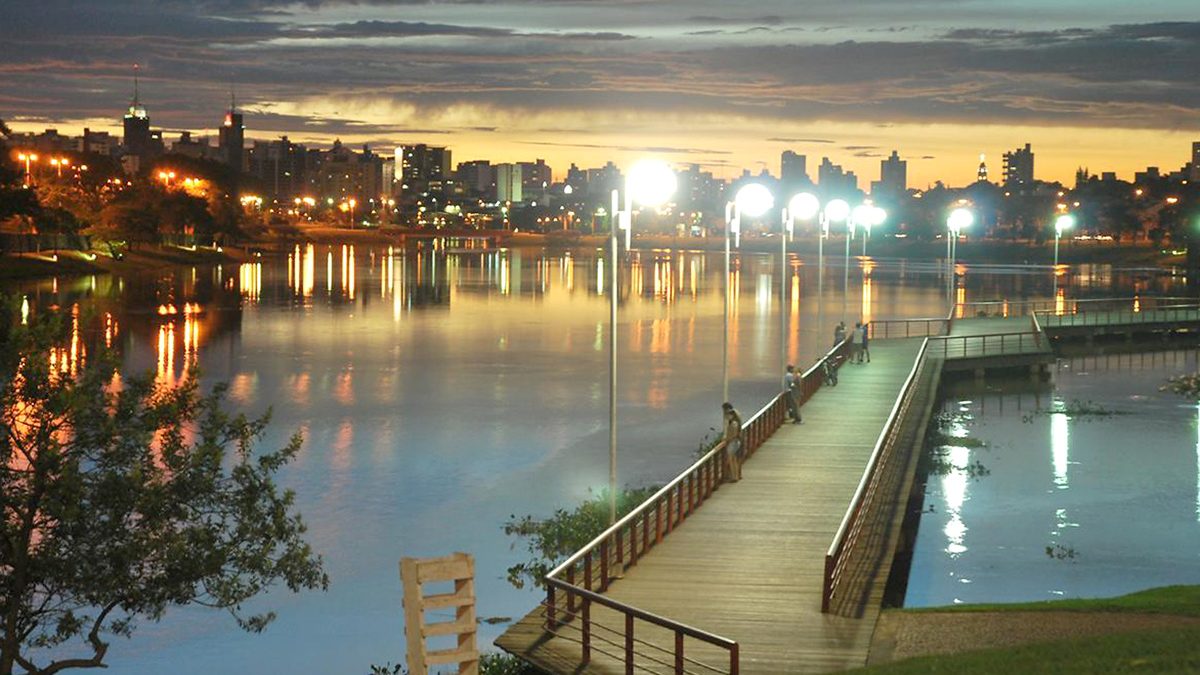Represa Municipal de São José do Rio Preto ao anoitecer, com deque de madeira e prédios iluminados ao fundo