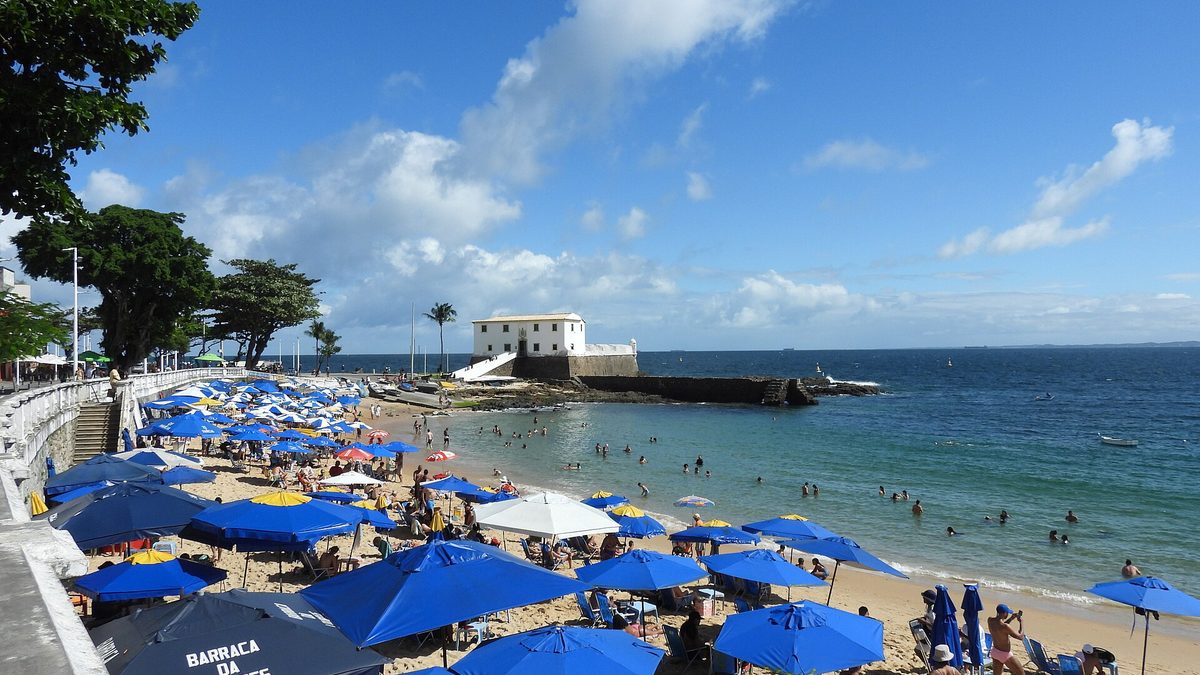 Guarda-sóis na areia do Porto da Barra, com o Forte de Santa Maria ao fundo, em Salvador
