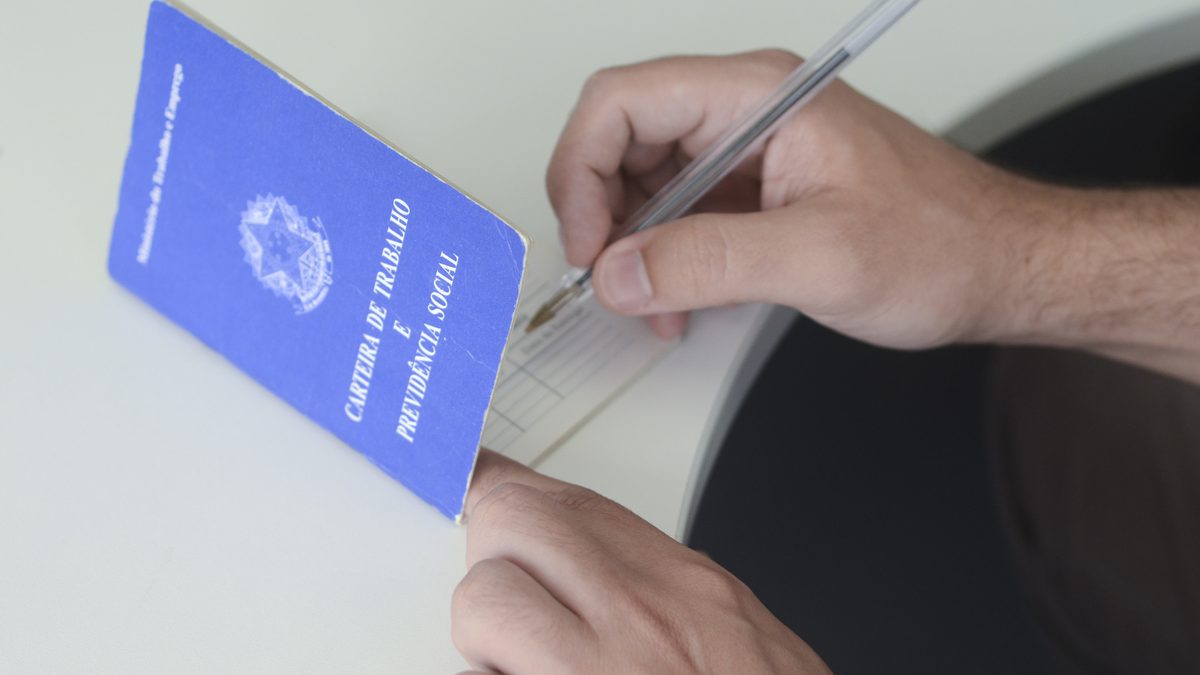 Mão preenche carteira de trabalho azul com caneta